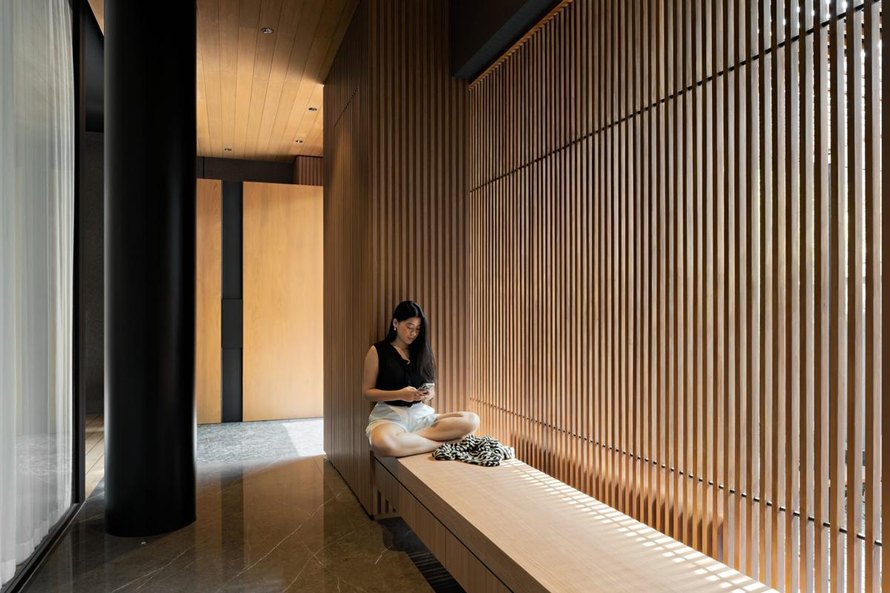 Koridor AD House dengan bangku kayu dan dinding kisi-kisi kayu