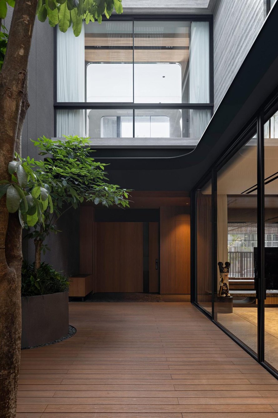 Courtyard hijau AD House dengan lantai kayu dan bukaan kaca besar