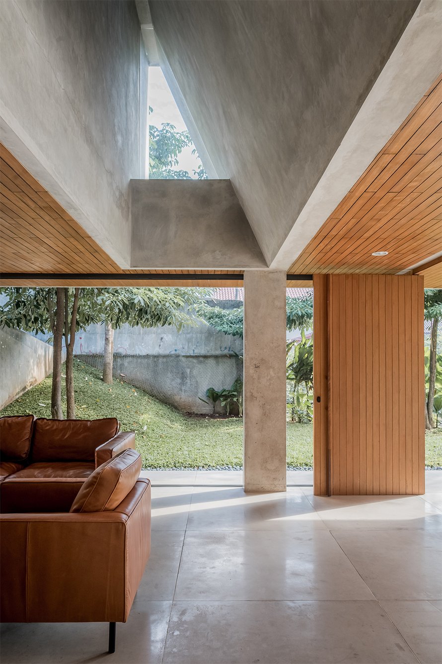 Void berkaca dan ruang keluarga Banjar House dengan furnitur kayu
