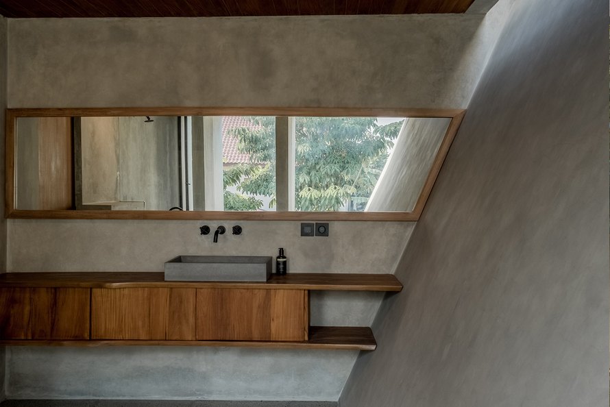 Ruang kamar mandi Banjar House dengan dinding miring, beton, dan kabinet kayu